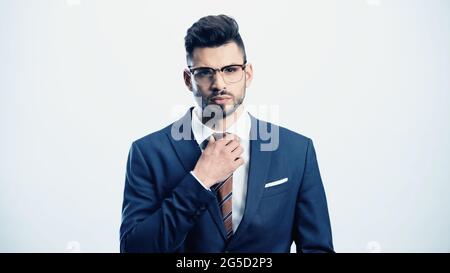 serious businessman touching tie while looking at camera isolated on white Stock Photo
