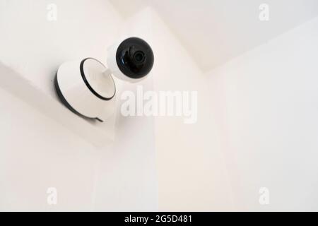 Modern indoor home security or surveillance camera installed on the wall. Home security concept, remote surveillance, surveillance. Stock Photo