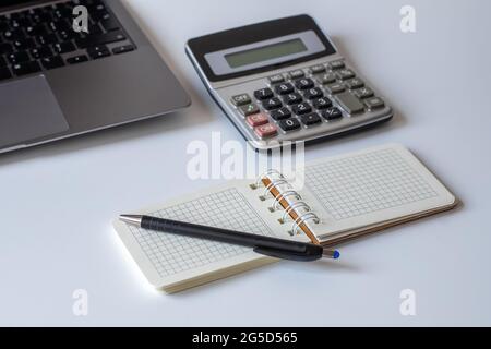 Office desk with spiral notepad, calculator, pen and laptop on white background Stock Photo