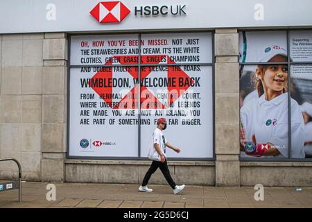 London, UK. 26th June, 2021. Pedestrians walk past an HSBC bank branch in Wimbledon town centre advertising the welcome  return of the 2021 Wimbledon Championships which is set to start on Monday 28 June. The  tennis  championships is back after it was cancelled  last year for the first time  since world war two due to the Covid-19 pandemic. Championship organizers have said that  capacity is reduced by 50% and spectators  must have pre-ordered tickets. Credit: amer ghazzal/Alamy Live News Stock Photo