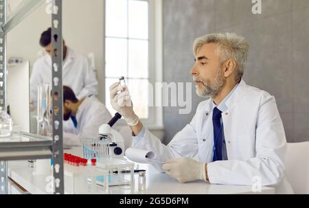 Serious scientist in lab coat and gloves working on new vaccine in medical laboratory Stock Photo