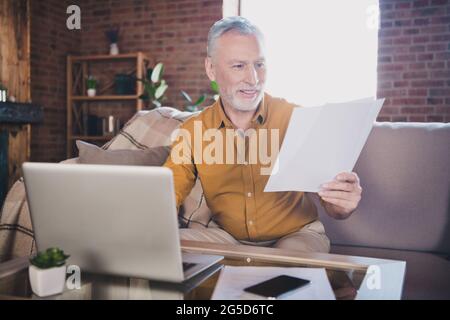 Photo of cheerful person sit on couch look arm hold paper document reading toothy smile have good mood indoors Stock Photo