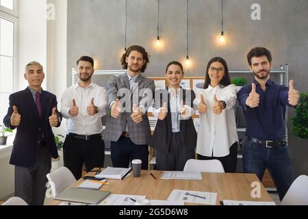 Team of happy company workers giving thumbs up after successful business meeting Stock Photo