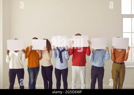 Group of people cover faces hiding behind white paper banners they are holding in hands Stock Photo