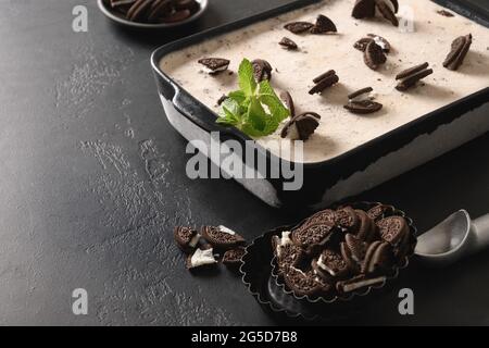 Homemade creamy ice cream with coffee cookies in container on a black background with copy space. Close up. Tasty children dessert without sugar. Stock Photo