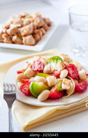 Salad with three kinds of tomatoes, boiled white kidney beans and croutons from white bread, with turkey stew on background Stock Photo