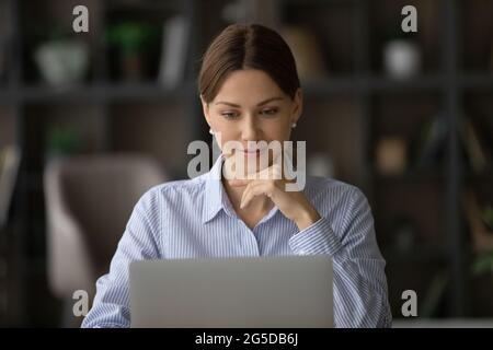 Smiling thoughtful young business lady working on computer. Stock Photo