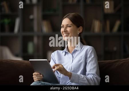 Happy dreamy young woman holding digital tablet in hands. Stock Photo