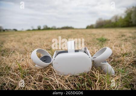 Oculus Quest 2 virtual reality headset with controllers, resting on a lawn Stock Photo
