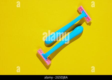 Two blue plastic razors on yellow background. Minimalistic beauty and fashion concept Stock Photo