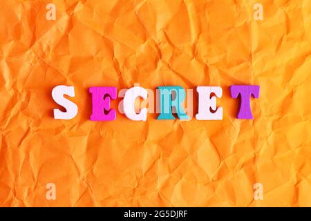 Colorful text SECRET on orange crumpled paper background Stock Photo