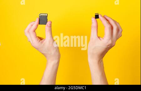 Female hands holds two SD memory cards on yellow background. Minimalist Techno Concept. Top view Stock Photo