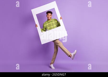 Full length body size of young man keeping photo frame cadre smiling on photo isolated on pastel violet color background Stock Photo