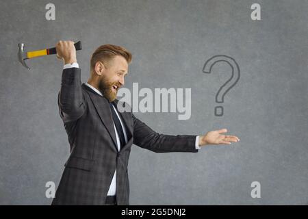 Businessman looking for answers to questions wants to crash question mark with hammer Stock Photo