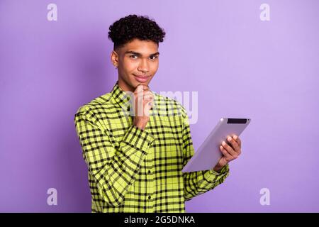 Portrait of attractive minded guy using tablet thinking deciding browsing web media isolated over violet purple color background Stock Photo