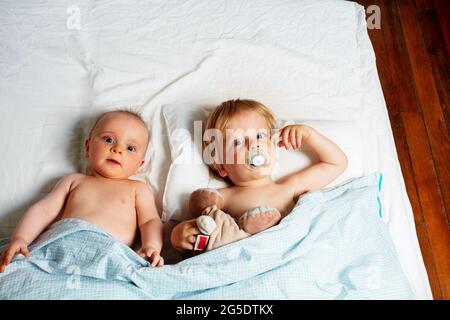 Little babies, boy and girl lay in a bed waking up Stock Photo