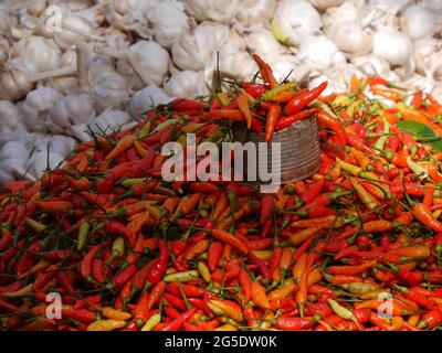 Fresh bright red spicy peppers and garlic cloves piled on market stall Stock Photo