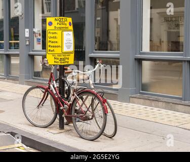 Parking suspended sign on a lamppost with two bicycles chained up underneath. London - 26th June 2021 Stock Photo