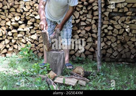 Lumberjack chopping wood with an ax in the yard and pile of cut stumps in the background on a summer day. Close up and copy space Stock Photo