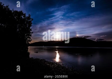 The Moon shinning through the clouds as it rises over the Hills by Ullswater in the English Lake District Stock Photo