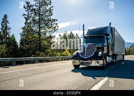Stylish black industrial long haul Big rig bonnet semi truck with chrome transporting frozen commercial cargo in refrigerator semi trailer running for Stock Photo