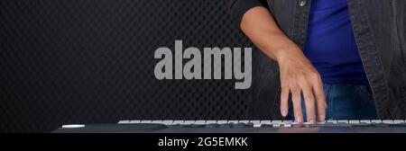 Closeup musician's hand playing on a music keyboard player in front of black soundproofing walls. Musician producing music in professional recording s Stock Photo