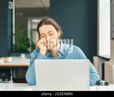 Tired male office worker falling asleep at work Stock Photo