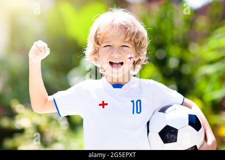 England football fan cheering. Kids play soccer and celebrate victory on outdoor field. England team supporter. Little boy in English jersey and cleat Stock Photo