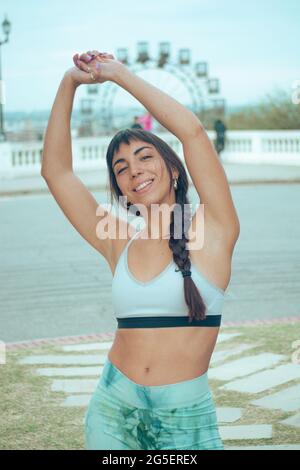 A vertical shot of a fit Argentine brunette stretching and smiling at the camera in a park Stock Photo