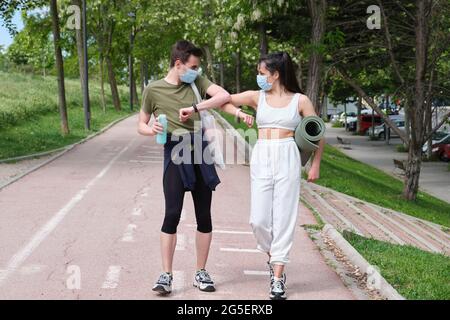 Young sport couple wearing protective face masks and greeting with elbows bumps for preventing corona virus spread. Fitness during coronavirus pandemi Stock Photo