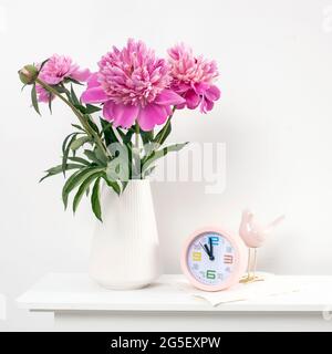 Red, pink peonies in a white vase on an table against a white wall background. Square frame Stock Photo