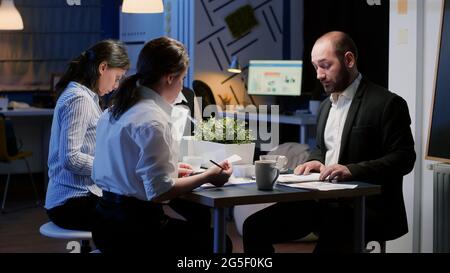 African american businesswoman planning company graphs presentation working in meeting room late at night. Diverse multi ethnic coworkers brainstorming strategy ideas solving graphs Stock Photo