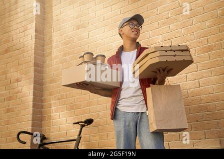 Young cheerful asian courier holding various packages with food, Stock Photo