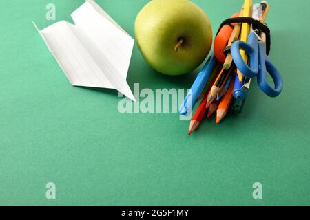 Bunch of school supplies with paper plane and apple on green background. Elevated view. Stock Photo