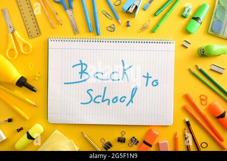 Open school line notebook in the center with back to school message and school supplies around on yellow background. Top view. Stock Photo