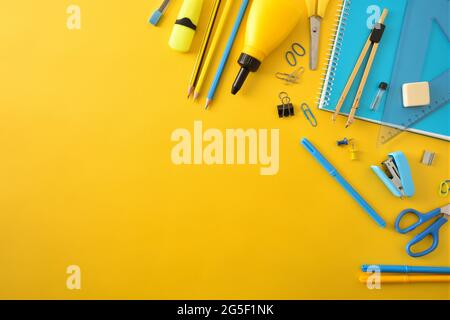 Yellow and blue school supplies on yellow background and top empty space. Top view. Diagonal composition. Stock Photo