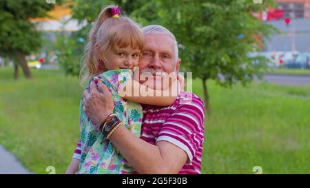 Little granddaughter child embracing kissing with her grandfather in park, happy family relationship Stock Photo