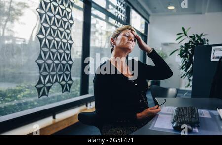 Stressed out businesswoman sitting at her desk rubbing her forehead and looking at computer. businesswoman with a hand on forehead. Stock Photo