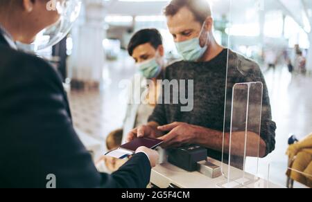 traveler man giving passport at check-in counter at airport during pandemic. Man standing at check-in counter at airport. Stock Photo