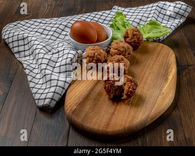 Meatballs on a wooden cutting board with two eggs and a salad leaf Stock Photo