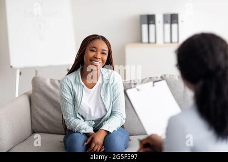 Successful therapy. Young female client having consultation with psychologist, grateful for professional help at clinic. Happy black lady speaking wit Stock Photo