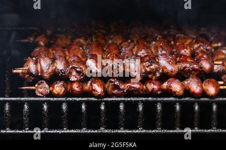 Close up searing and smoking glazed chicken yakitori hearts on wooden skewers on open fire outdoor grill with metal grate, high angle view Stock Photo