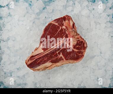 Close up one aged prime marbled raw porterhouse T bone beef steak on background of crushed ice on retail display, elevated top view, directly above Stock Photo