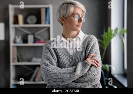 White-haired focused woman looking aside while standing in office Stock Photo