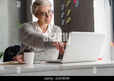 White-haired young woman smiling and pointing finger at laptop in office Stock Photo