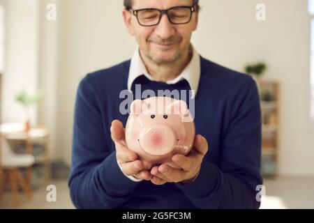 Elderly man pensioner with eyes closed holding piggy bank in hand portrait Stock Photo