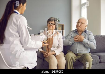 Mature couple sitting on a sofa talking and consulting about health with a doctor during her visit. Stock Photo