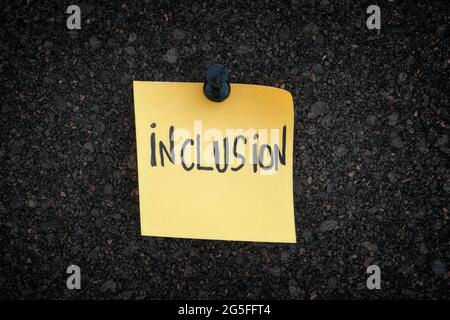 Inclusion. The word Inclusion written on a yellow paper note pinned to a cork board. Close up. Stock Photo