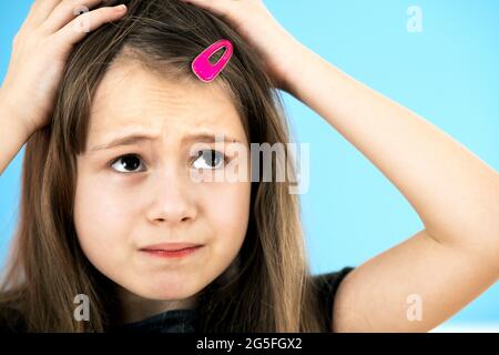 Close up portrait of upset and pensive little girl with cute pink hairpin on blue background. Stock Photo