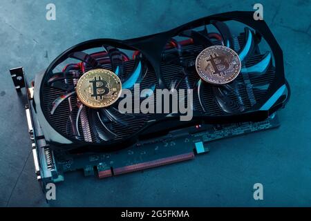 Gold bitcoin coins lie on the cooler of a powerful video card with cyanide neon illumination. Stock Photo
